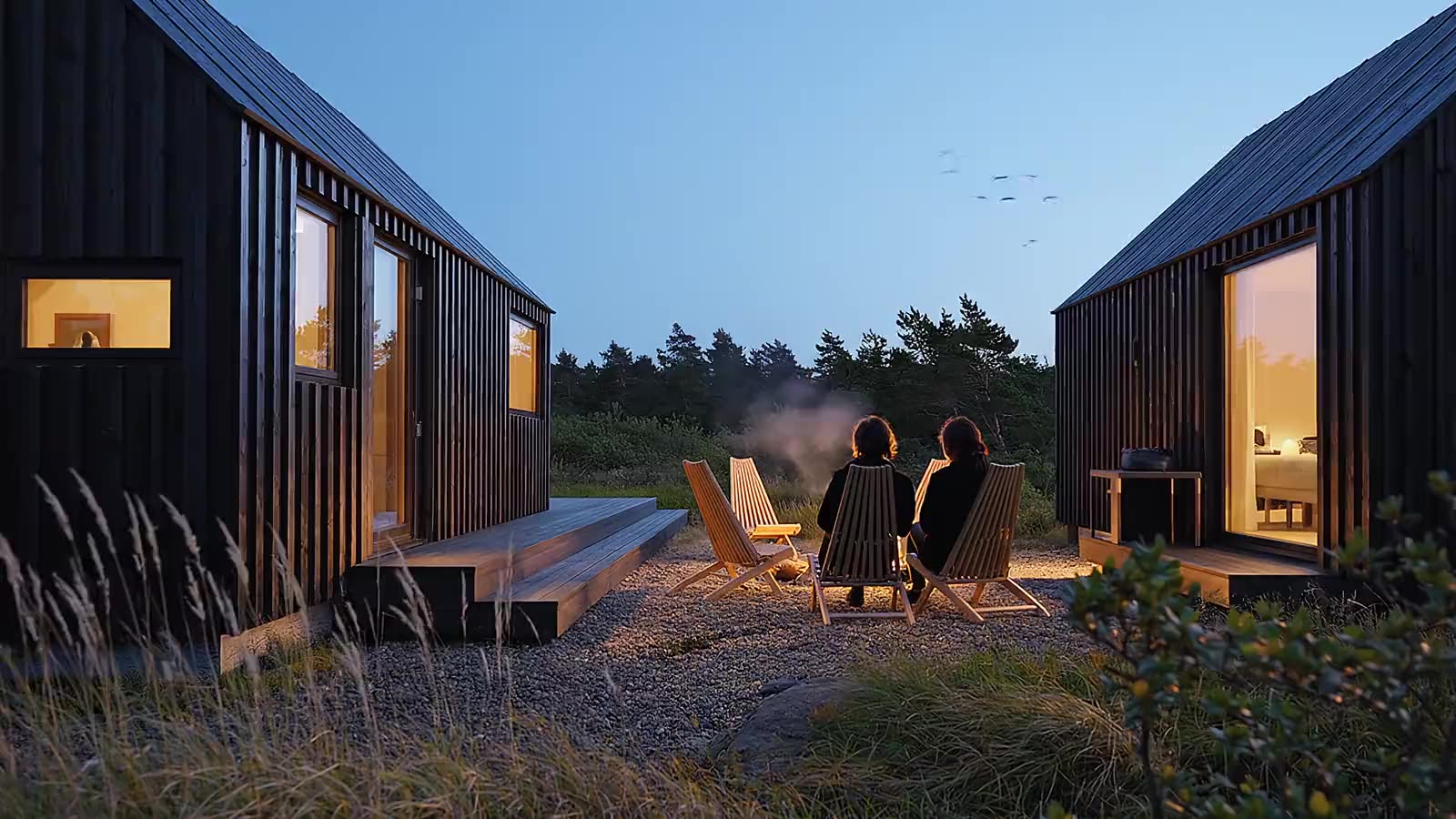 Rendering di esterni 3D di baite in legno nero al crepuscolo, due persone sedute accanto a un braciere, Norvegia