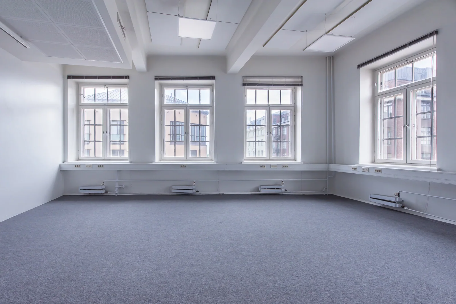 Una sala de reuniones vacía con moqueta azul, cuatro ventanas altas y calefactores de pared, tal como fue fotografiada, Finlandia